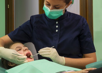 Mujer dentista examinando los dientes de una niña. - obrazy, fototapety, plakaty