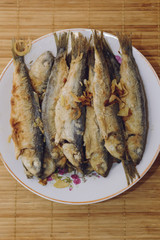 Fried fish Baltic herring lies on a plate on a bamboo napkin.