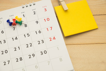 top view. pin putting on desktop calendar and have post-it note put on beside them. wooden are background. this image for business accessory concept