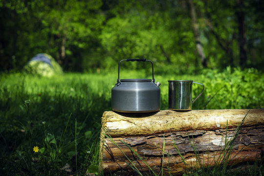 Kettle and mug on the log in sunny spring day with forest and tent background © dwhome