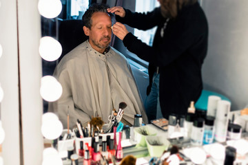 Backstage man sitting in front of mirror getting make-up.