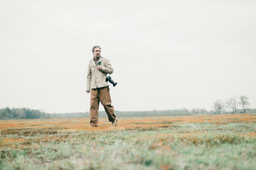 Man with camera walking over grassy land.