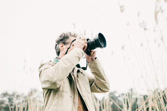 Man taking pictures of nature. Standing between reed.