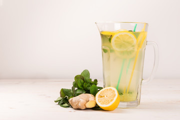 A glass decanter with a summer refreshing lemonade made of lemons and ginger with mint added on a white wooden background. Detox water. Ingredients. Cleaning the body of toxins, vitamins