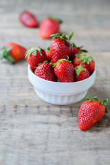 Ripe red fresh strawberry on a rustic wooden table in white bowl
