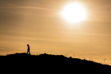 Man walking away from the sun on the hill. Artistic silhouette retro edit.