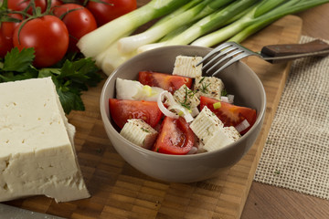 tomatoes and cheese salad with vegetables on wooden background