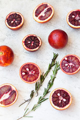 Red Sicilian orange whole and cut on a light background with branches of rosemary. Daylight, open space for your text.