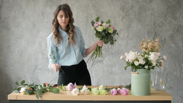 Florist at work: pretty young blond woman holds fashion modern bouquet of different flowers with peone and roses in craft paper