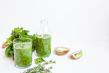 Green cocktail in a bottle and in a glass with spinach, mint, rosemary, kiwi and apple on a light background.