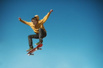 A teenager skateboarder does an ollie trick on background of blue sky gradient - obrazy, fototapety, plakaty