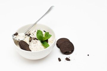 Homemade vanilla ice cream in a ceramic bowl with chocolate chip cookies and mint on a white background.