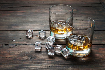 Two glasses of whiskey with ice cubes served on wooden planks. Vintage countertop and a glass of hard liquor