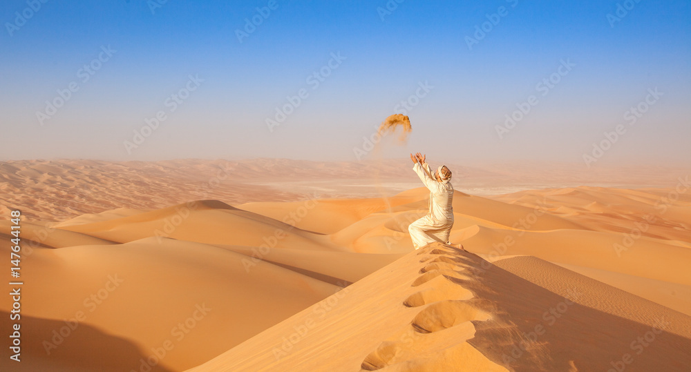 Wall mural arab man in local outfit playing with sand in the  arabian Desert