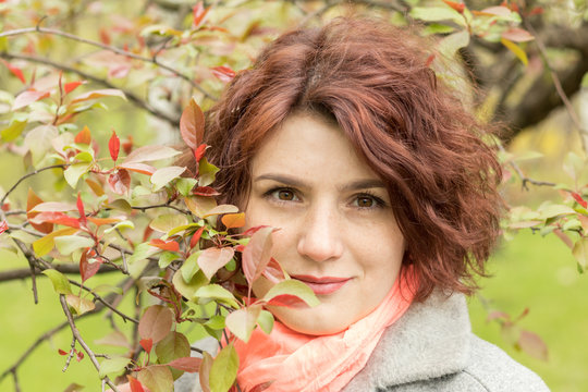 Pretty romantic young red head woman with apple branches red leaves in spring park. Spring trees background. Portrait close up.