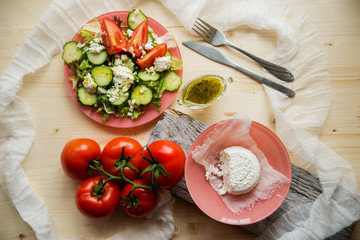 Greek salad in a glass salad bowl among ingredients for its cooking on an old wooden surface