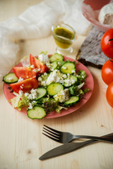 Greek salad in a glass salad bowl among ingredients for its cooking on an old wooden surface