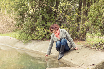 Pretty romantic young red head woman sitting close to the pond in spring park. Spring trees background.