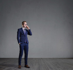 Businessman with smartphone standing in front of a grey wall. Business, office, concept.