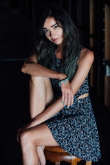 Fototapeta premium A charming young girl in a dress is sitting on a wooden chair in a cafe. Dark background.
