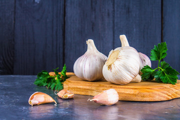 Garlic cloves and garlic bulb on a wooden board on a gray background.