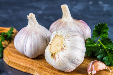 Garlic cloves and garlic bulb on a wooden board on a gray background.