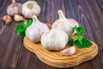 Garlic cloves and garlic bulb on a wooden board on a brown background.