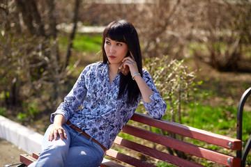 Beautiful asian appearance girl sitting on bench in park and talking on phone