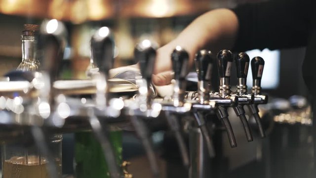 Close up of bartender s hands cleaning a row of taps with beer kegs in a bar. Handheld real time close up shot
