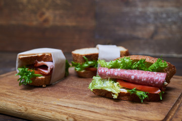 Sandwiches with two slices of lettuce and bread, one of sausage and tomato wrapped in paper