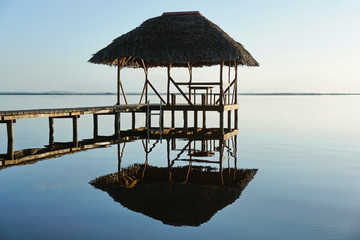 Thatched hut overwater and its reflection on a calm water surface, sunrise light, natural scene, Caribbean sea, Panama, Central America