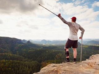 Hiker huts knee. Man with leg in join immobilizer stay on summit and raise medicine cruth above head.