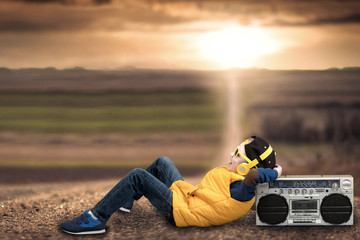 Boy style hip-hop, listening to vintage tape recorder, lying on a country road.
