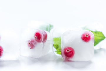 frozen red berries in ice cubes with mint on stone background
