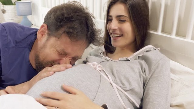 Couple in love expecting baby laughing and smiling in bed in the morning closeup