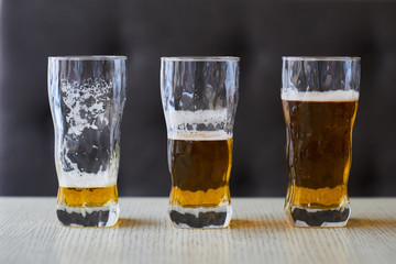 Three glasses of light beer on table. One full glass of beer, one half and one empty.