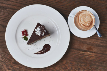 Cup of cappuchino coffee and piece of chocolate poppy cake on wooden table. Flatlay or top view.