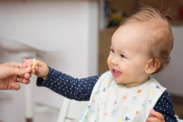 One year old baby girl feeding herself with her fingers, baby led weaning; concept of motherhood and parenting