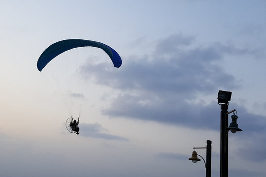 Silhouette of a male paraglider on a paraplan against a background of a sunset in the sky and clouds hovering over the sea. Concept: freedom, loneliness, hobby, sport.