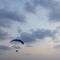 Silhouette of a male paraglider on a paraplan against a background of a sunset in the sky and clouds hovering over the sea. Concept: freedom, loneliness, hobby, sport.