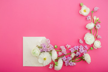 Beautiful spring flowers and paper envelope on pink background. Flat lay, top view. Floral frame