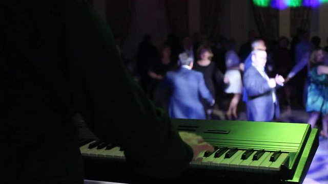 A musician in the foreground plays a keyboard instrument for dancing business people.