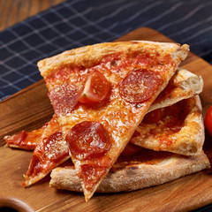 Several slices f pepperoni pizza and cherry tomatoes lying on wooden board on table