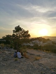 Two young lovers watching the sunset on the top of Athens city mountain