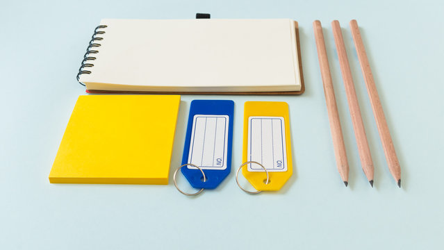 Notebook place on blue background with yellow post it, pencils and plastic tags