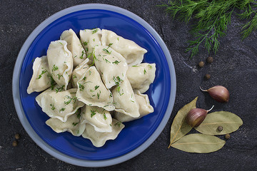 Traditional russian pelmeni or dumplings with meat in a blue plate  on black concrete background.