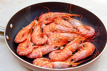 Large orange shrimp stir-fried in a skillet with garlic.
