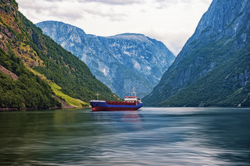 Norwegian fjord surrounded by mountains with sailing ship in a cloud summer day horizontal frame