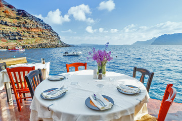 Traditional Greek tavern with orange wooden chairs by the seashore of Aegean sea, Greece, Santorini island in Cyclades. Luxury background.