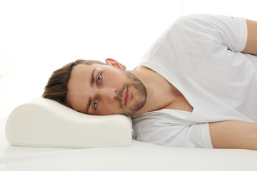 Young man lying on bed with orthopedic pillow against white background. Healthy posture concept